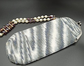 May include: A silver beaded purse with a white and gray striped pattern. The purse has a silver clasp and a beaded chain with white and purple beads.