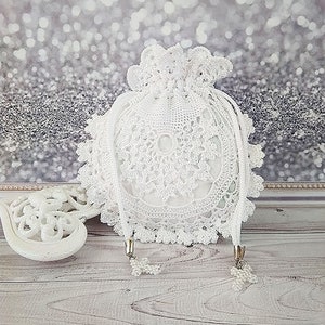 Puede incluir: Bolsa de cordón de ganchillo blanco con un delicado patrón de encaje y borlas de cuentas.