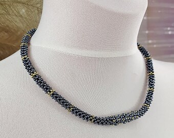 May include: A black and gold beaded necklace with a simple design. The necklace is made of small, round beads that are strung together in a continuous pattern. The beads are interspersed with gold beads, which add a touch of elegance to the piece.