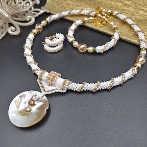 May include: A white and gold beaded necklace set with a large iridescent shell pendant. The set includes a matching bracelet and earrings.