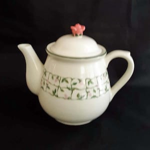 May include: A white teapot with a green and pink floral design and a pink rosebud on the lid.