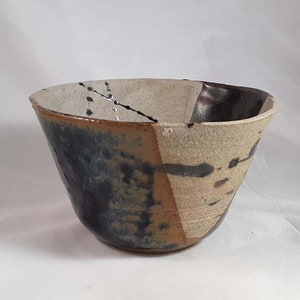 May include: A ceramic bowl with a white, brown, and black glaze. The bowl has an abstract design with splashes of color and black lines.