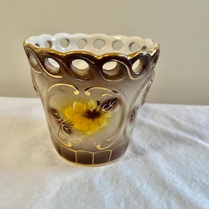 May include: A small, brown and white ceramic planter with a yellow flower design. The planter has a scalloped rim with cut-out holes.