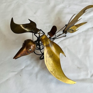 May include: A vintage metal bird sculpture with a copper head and beak, brass wings, and a dark metal frame. The sculpture has a unique, abstract design and is set against a white background.