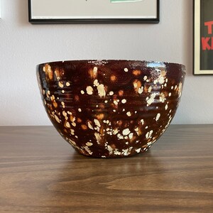 May include: A brown ceramic bowl with white speckles. The bowl is round and has a wide rim.