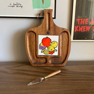 May include: A wooden cheese board with a tile featuring a colorful illustration of fruit. The board has four sections and a small knife is included.
