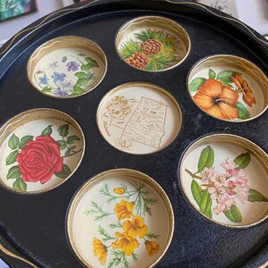 May include: A black tray with seven round, gold-rimmed compartments, each featuring a different floral design. The tray is perfect for serving drinks or snacks.