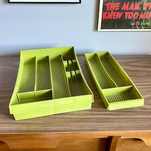 May include: Two lime green plastic utensil trays with multiple compartments. The trays are rectangular with a mesh-like pattern on the bottom. One tray is larger and has a section for knives, forks, and spoons. The other tray is smaller.