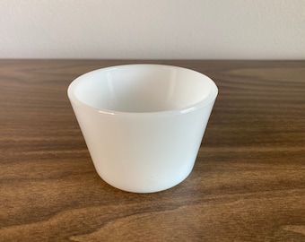 May include: A white ceramic cup with a rounded bottom and a slightly flared rim.
