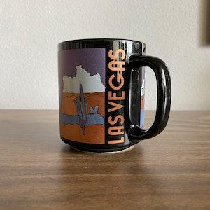 May include: Black ceramic mug with a colorful illustration of a desert landscape and the text "LAS VEGAS" on the side.