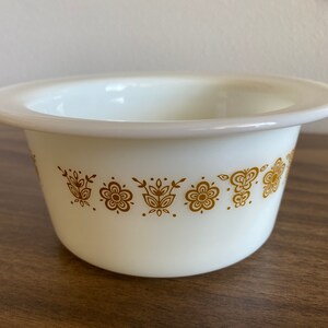 May include: White ceramic bowl with a gold floral pattern around the rim. The bowl is round and has a slightly flared lip.