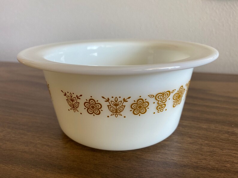 May include: White ceramic bowl with a gold floral pattern around the rim. The bowl is round and has a slightly flared lip.