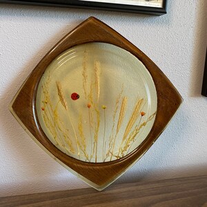 May include: A round, clear resin tray with a wooden frame. The tray contains pressed flowers and a ladybug.