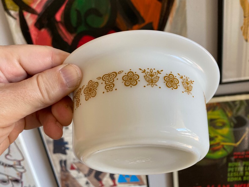 May include: White ceramic bowl with a gold floral pattern around the rim. The bowl is slightly angled and the rim is slightly raised.