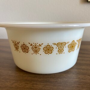 May include: White ceramic bowl with a gold floral pattern around the rim. The bowl is round and has a slight lip.