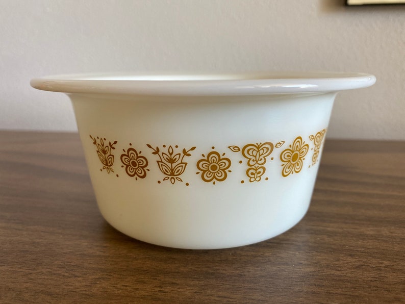 May include: White ceramic bowl with a gold floral pattern around the rim. The bowl is round and has a slight lip.