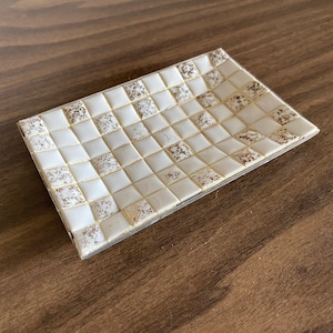 Puede incluir: Un jabonera de cerámica blanca con un diseño de mosaico dorado. La jabonera es rectangular y tiene un borde ligeramente elevado.