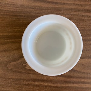 May include: A white ceramic bowl with a smooth, rounded rim. The bowl is empty and has a slight sheen.