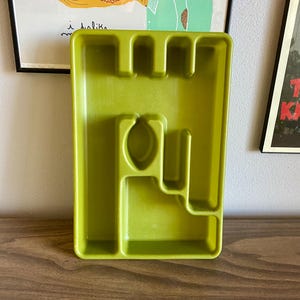 May include: A green plastic cutlery tray with four compartments. The tray has a unique design with a raised section in the center.