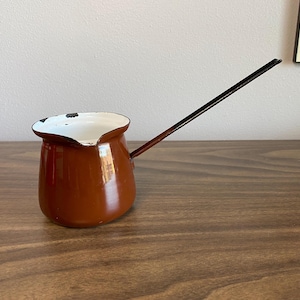 Op de afbeelding: Een bruine emaille koffiepot met een wit interieur en een zwarte handgreep. De pot heeft een afgeronde vorm en een tuit.