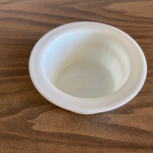 May include: A white ceramic bowl with a raised rim. The bowl is empty and has a smooth, glossy finish.