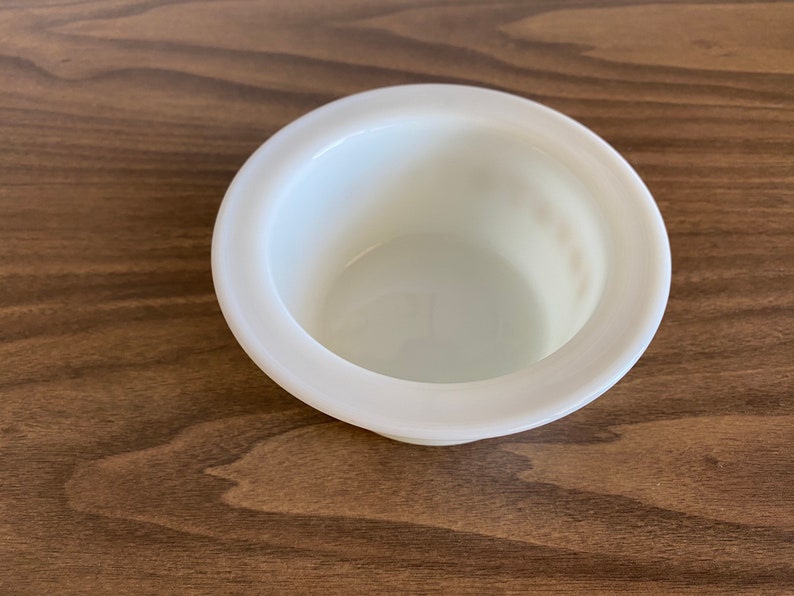 May include: A white ceramic bowl with a raised rim. The bowl is empty and has a smooth, glossy finish.