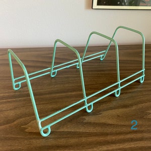 May include: A light blue metal wire rack with four compartments. The rack is designed to hold plates or other flat items.