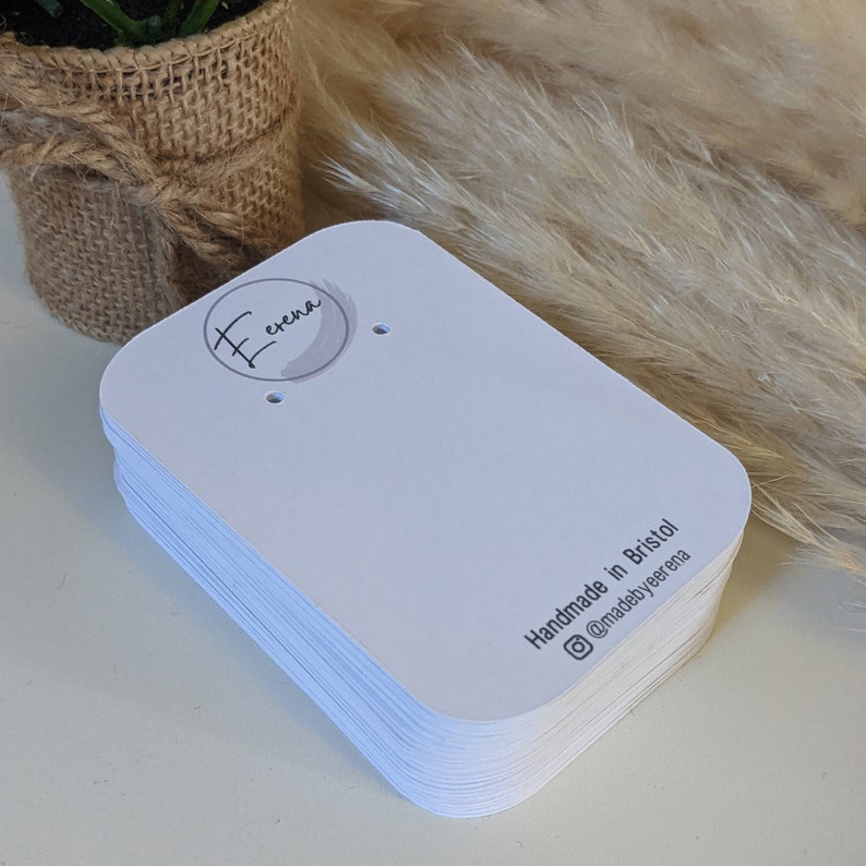 Puede incluir: Una pila de tarjetas de exhibici&oacute;n de aretes blancas con esquinas redondeadas. Las tarjetas tienen un c&iacute;rculo peque&ntilde;o con la palabra "erena" escrita en cursiva y un dise&ntilde;o similar a la acuarela. La parte posterior de las tarjetas dice "Handmade in Bristol @madebyerena".