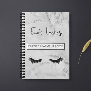 Puede incluir: Una libreta de mármol blanco con una encuadernación en espiral negra. La portada presenta el texto "Eva's Lashes" y "CLIENT TREATMENT BOOK" en negro. Hay dos pestañas negras dibujadas en la portada.