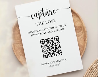 May include: A white sign with black text: "capture THE LOVE SHARE YOUR PHOTOS WITH US SIMPLY SCAN AND UPLOAD." A QR code is below the text, and the names "GERRY AND MARTYN" and the date "14.06.2025" are at the bottom. The sign is on a wooden plate.