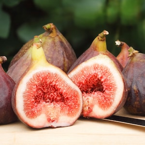 Peut inclure: Un groupe de six figues mûres, dont certaines sont coupées pour révéler leur chair rouge, sur une planche à découper en bois. Un petit couteau est posé à côté des figues.