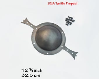 May include: A dark grey metal shield boss with a central dome and two pointed, decorative extensions on opposite sides. The circular plate features pre-drilled holes for mounting, accompanied by a small set of matching metal rivets. Measures 12.75 inches.