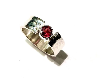 May include: A silver ring with a hammered finish and a red gemstone set in the center.