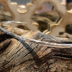 Peut inclure: Un bracelet jonc en argent martelé avec une finition lisse et polie. Le bracelet est ouvert et présente un design simple et minimaliste.