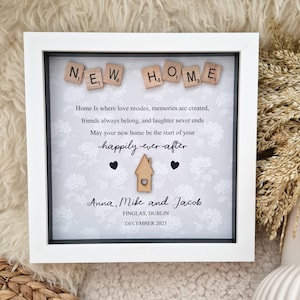 May include: A white picture frame with a gray background and a message about a new home. The message reads "NEW HOME" with wooden letter tiles. The message continues, "Home is where love resides, memories are created, friends always belong, and laughter never ends. May your new home be the start of your happily ever after." The frame also includes the names "Anna, Mike and Jacob", the location "FINGLAS, DUBLIN", and the date "DECEMBER 2023".