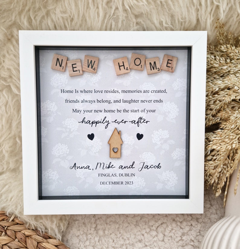 May include: A white picture frame with a gray background and a message about a new home. The message reads "NEW HOME" with wooden letter tiles. The message continues, "Home is where love resides, memories are created, friends always belong, and laughter never ends. May your new home be the start of your happily ever after." The frame also includes the names "Anna, Mike and Jacob", the location "FINGLAS, DUBLIN", and the date "DECEMBER 2023".