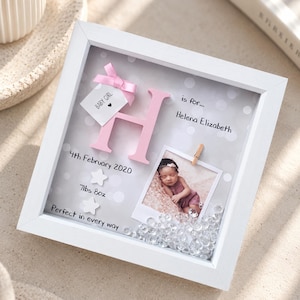 Op de afbeelding: Een witte schaduwdooslijst met een roze letter H, een babyfoto vastgeklemd aan de achtergrond en de tekst H is for... Helena Elizabeth, 4th February 2020, 7lbs 8oz, Baby Girl, Perfect in every way, met doorzichtige kristallen.