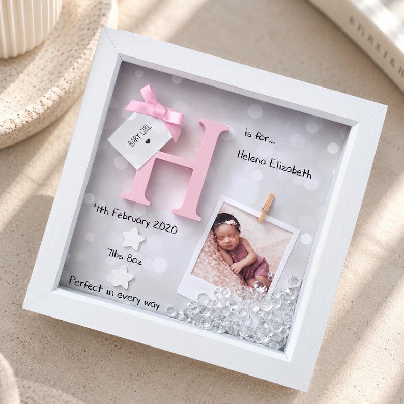 Op de afbeelding: Een witte schaduwdooslijst met een roze letter H, een babyfoto vastgeklemd aan de achtergrond en de tekst H is for... Helena Elizabeth, 4th February 2020, 7lbs 8oz, Baby Girl, Perfect in every way, met doorzichtige kristallen.