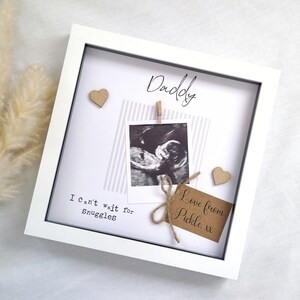 May include: White picture frame with a black and white ultrasound image, two brown paper hearts, a brown paper tag with the text "Love from Pickle, xx" and the text "Daddy" and "I can't wait for snuggles".