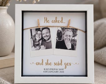 Peut inclure: Un cadre carré blanc de type boîte contenant deux photos noir et blanc style polaroïd fixées sur une ficelle. Le texte indique He asked... and she said yes, suivi des prénoms Kayleigh & Sam et de la date 6th January 2024.