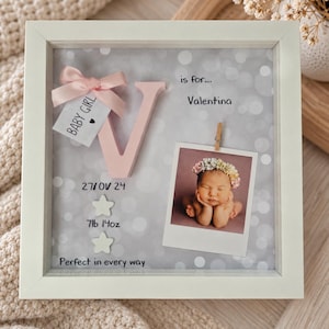 Op de afbeelding: Een witte vierkante schaduwdooslijst met een roze letter V, een kleine roze strik en een label met BABY GIRL. Het bevat een babyfoto, de tekst is for... Valentina, 27/01/24, 7lb 14oz, en Perfect in every way, met twee ster-pictogrammen.