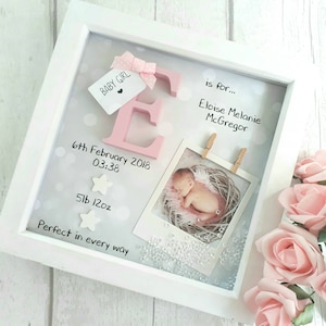 Op de afbeelding: Een witte schaduwdooslijst met een roze letter E met strik, een foto van een baby in een nestje en de tekst Baby Girl, is for Eloise Melanie McGregor, 6th February 2018, 03:38, 5lb 12oz, en Perfect in every way, met sterren als accenten.