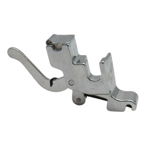 May include: A silver sewing machine foot with a lever and a roller. The foot is designed for sewing a rolled hem.