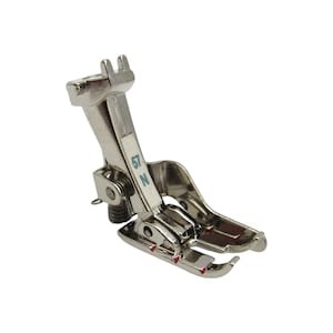 May include: A silver sewing machine foot with a red marking and the number "57 N" printed on the side.