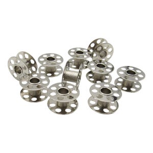 May include: A set of ten silver metal bobbins for a sewing machine. The bobbins are arranged in a circle on a white background.