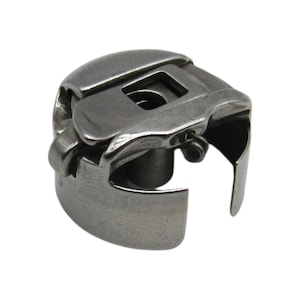 May include: A silver metal bobbin case for a sewing machine.