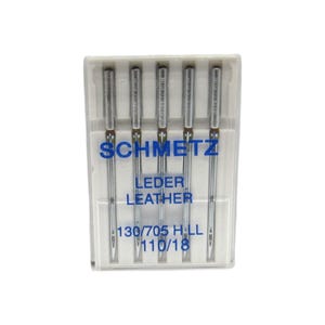 May include: A pack of five silver sewing needles in a clear plastic case. The needles are labeled "Schmetz Leder Leather 130/705 HLL 110/18".
