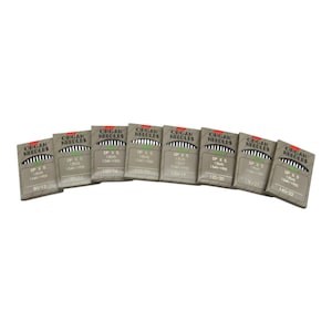 May include: Eight packages of Organ needles for sewing machines. The packages are brown with white text and are arranged in a semi-circle. The text on the packages reads "Organ Needles" and "DP X 5" with various needle sizes listed, such as 80/12, 100/16, 110/16, 120/19, 125/20, 130/21, and 140/22.