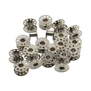 May include: A pile of silver metal sewing machine bobbins. The bobbins are round with a hole in the center and a series of small holes around the edge.