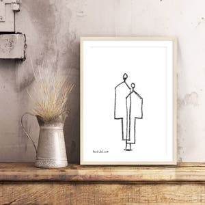 May include: Black and white line drawing of two figures standing side by side. The drawing is framed in a light wood frame and is on a wooden surface.